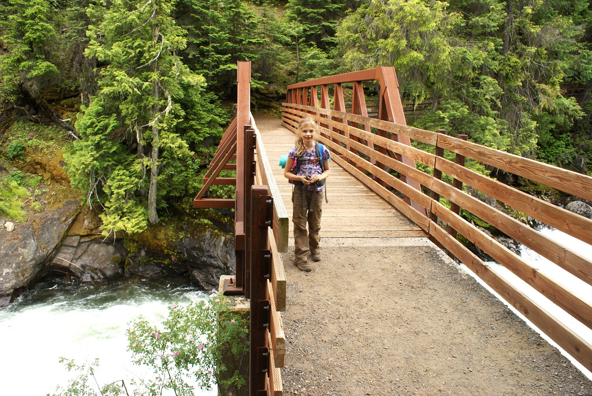 A girl hiker with a backpack poses on a footbridge across the Icicle Gorge near Leavenworth, among best wildflower hikes near Seattle