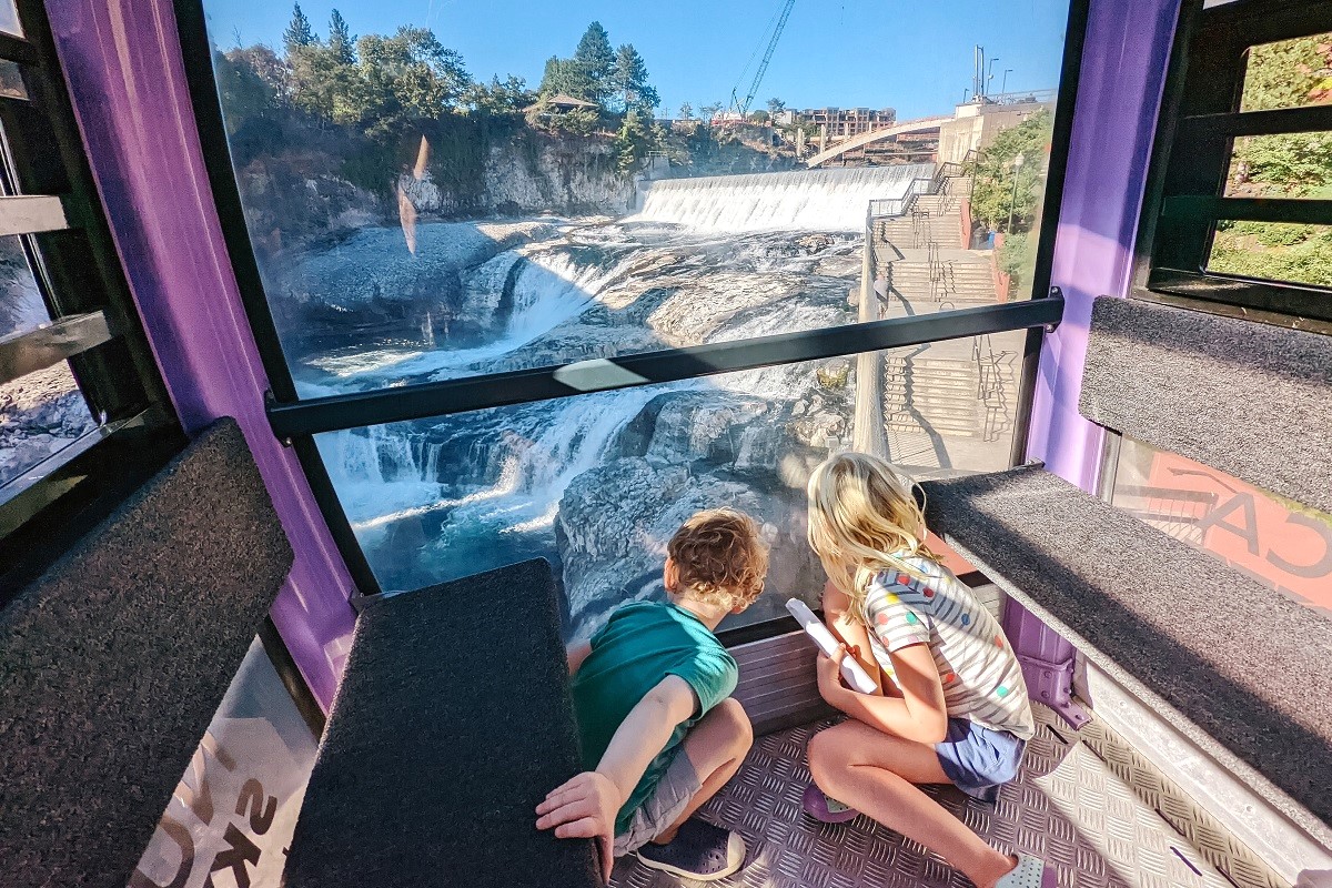 Two children looking through a window at Spokane Falls from the Numerica Sky Ride over the Spokane River