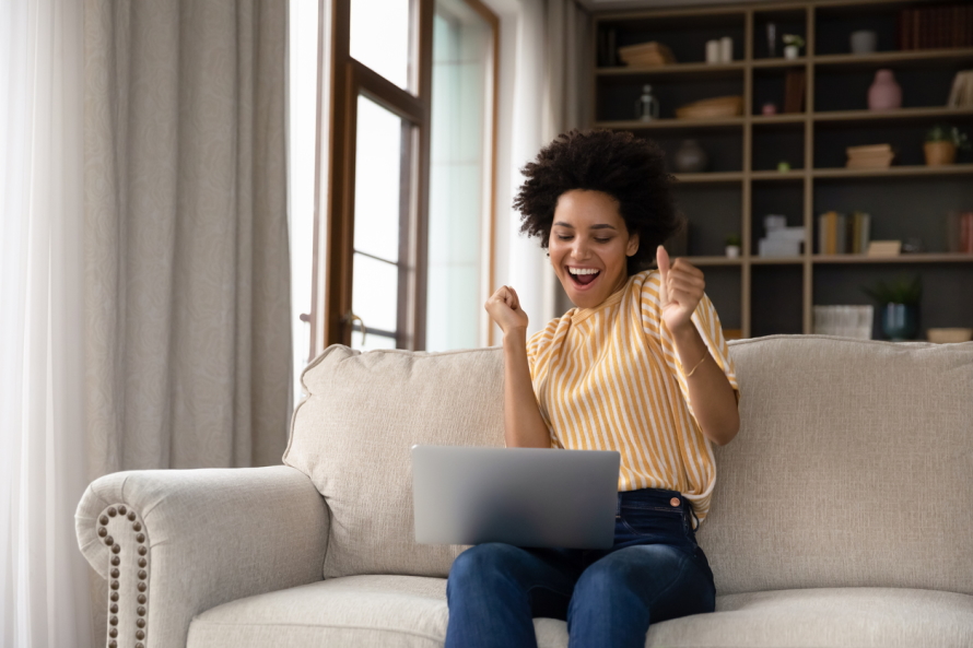 woman sitting on couch looking exciting holding a laptop