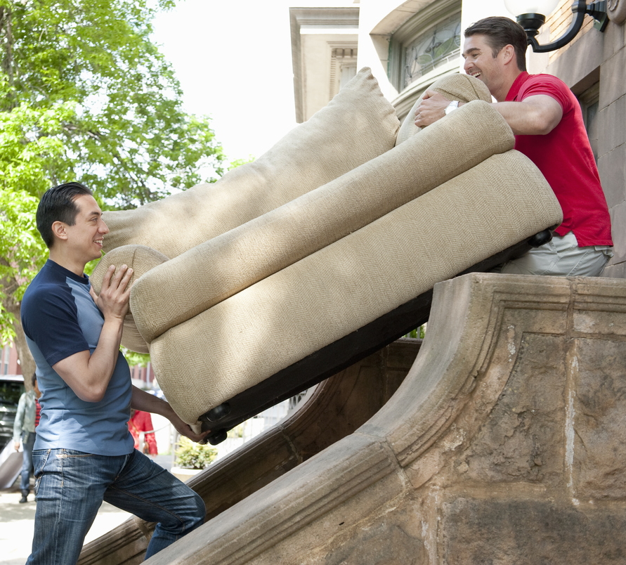 Two men carrying a couch down some stairs