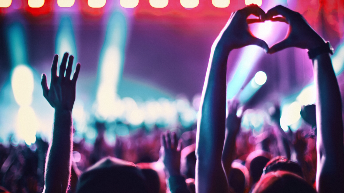 Teens at a live concert with hands raised in the air 
