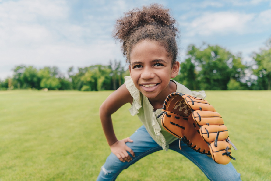 Young girl standing in a field wearing a baseball glove