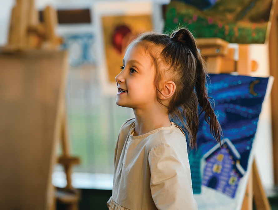 Young girl looking excited standing in front of painting canvas 