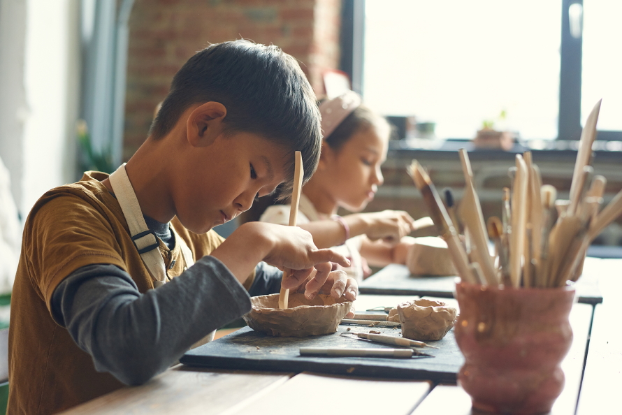 Young boy sitting at a table making a bowl out of clay