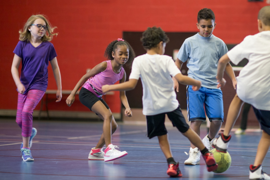 group of kids playing soccer in a gym