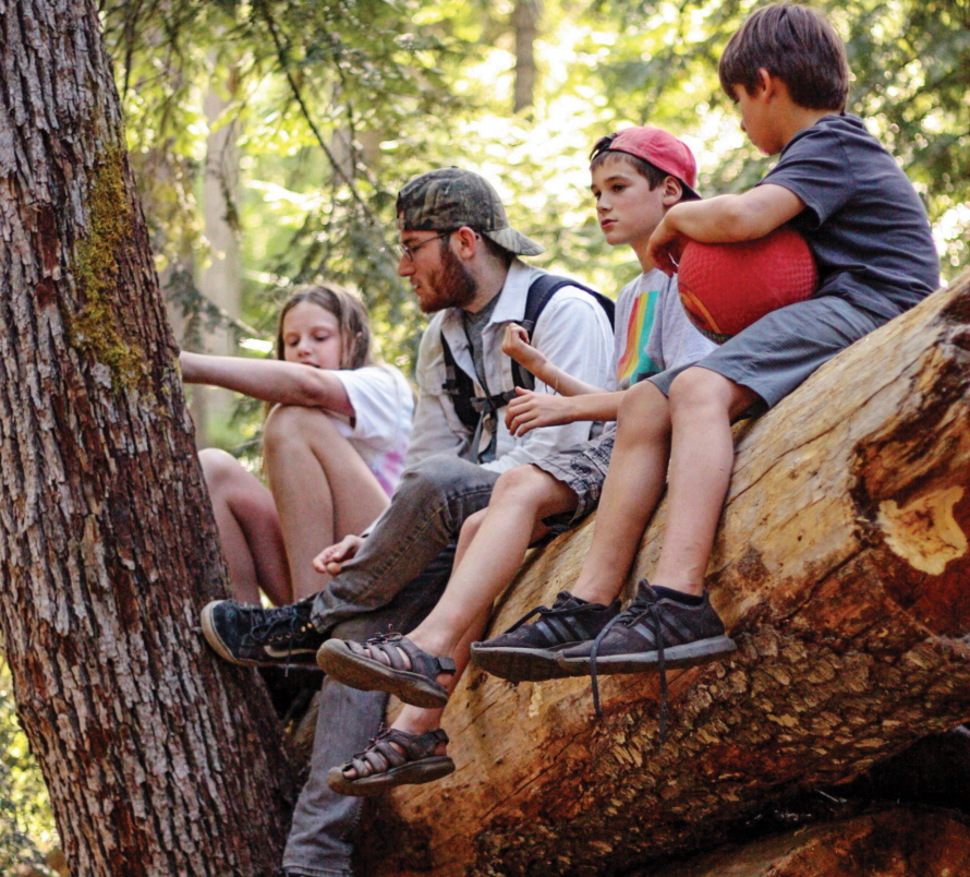 Kids sitting on a fallen tree with a camp counselor 