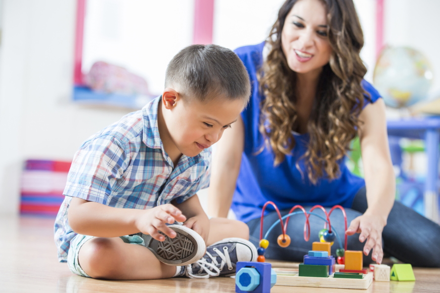 Young boy sitting on the floor playing with toys next to smiling woman