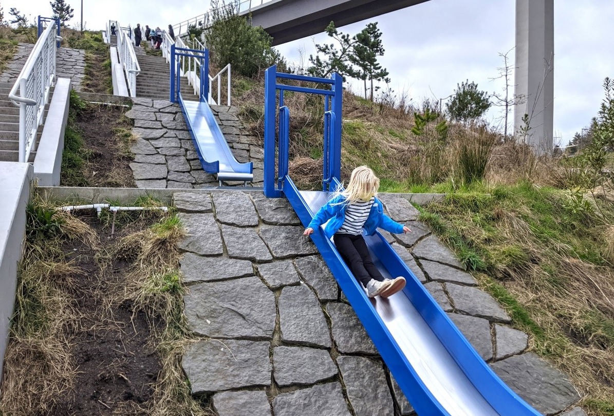 A girl slides down one of the series of hillside slides at the newer section of Tacoma's point defiance park called Dune Peninsula among fun adventure playgrounds in the greater Seattle area
