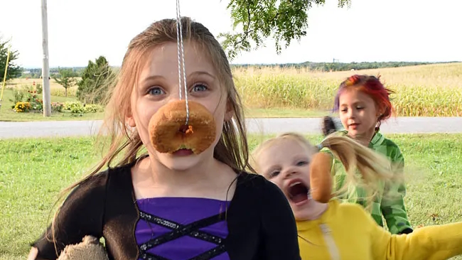 Girl eating a donut on a string is a delicious Halloween party game kids love to play