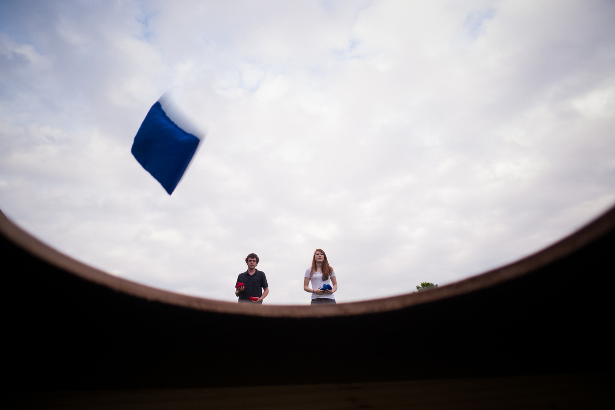 View from inside a corn hole set as two kids throw a bean bag.