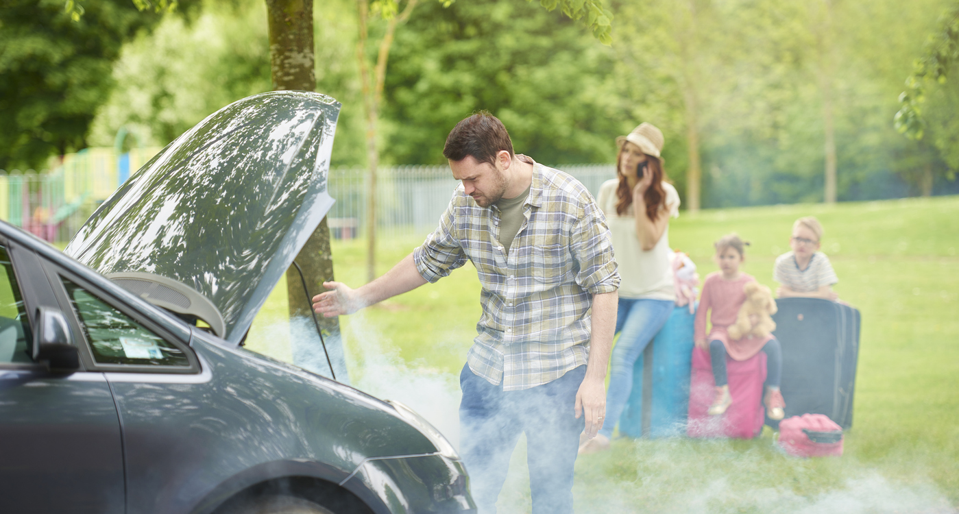 Smoke floats out from under a car hood while a stressed family looks on.