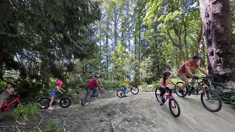 Families ride bikes through the Cedar Lanes Park pump track, a Seattle-area bike pump track