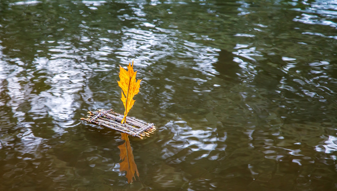 small raft made out of sticks with a yellow leaf on top acting as a sail