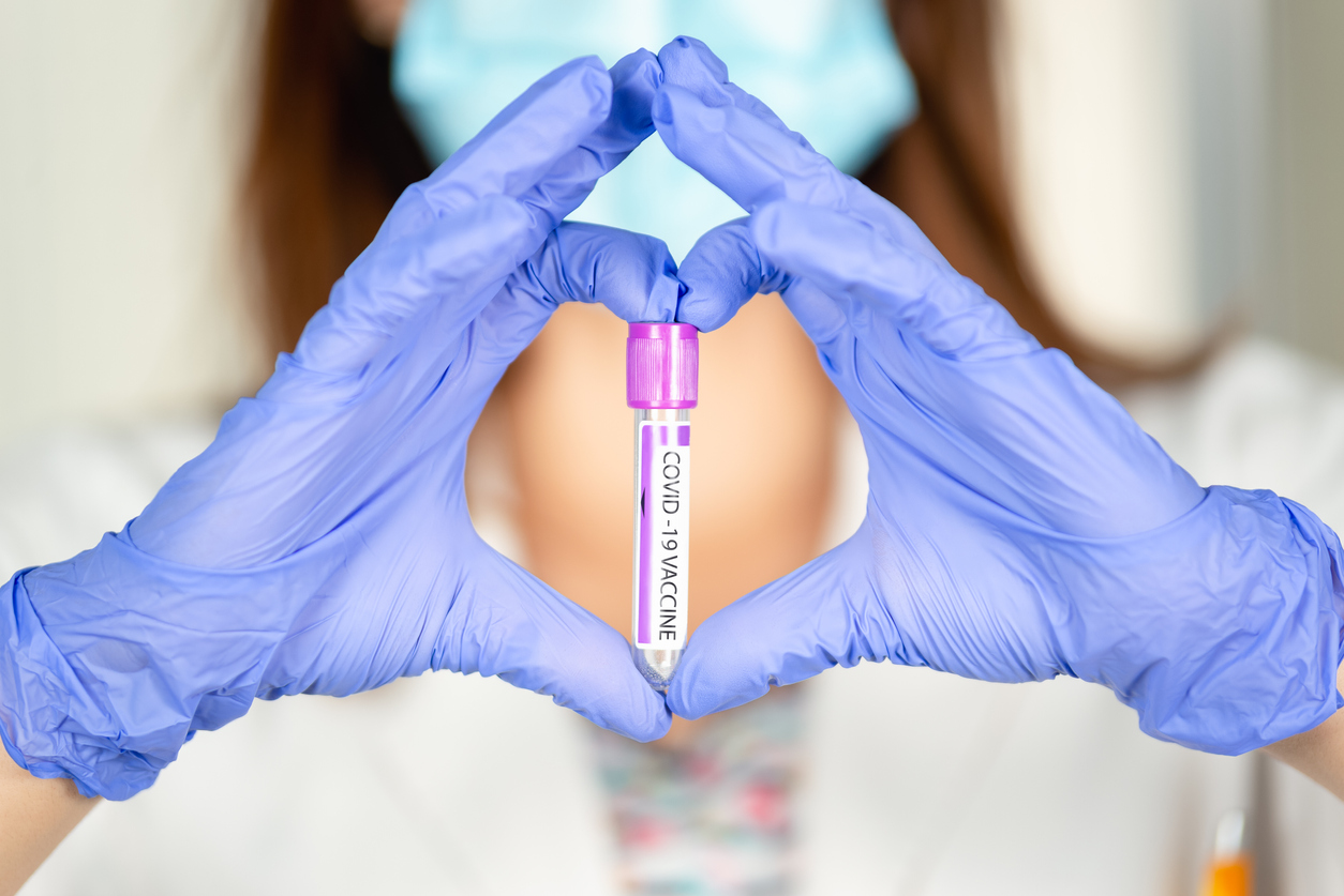 gloved hands making the shape of a heart around a vial with a covid vaccine label
