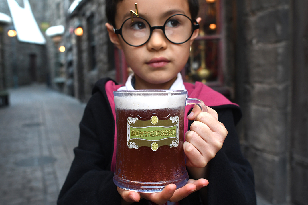 A boy dressed in a Hogwarts robe holds a mug of Butterbeer at Wizarding Wold of Harry Potter top tips for families