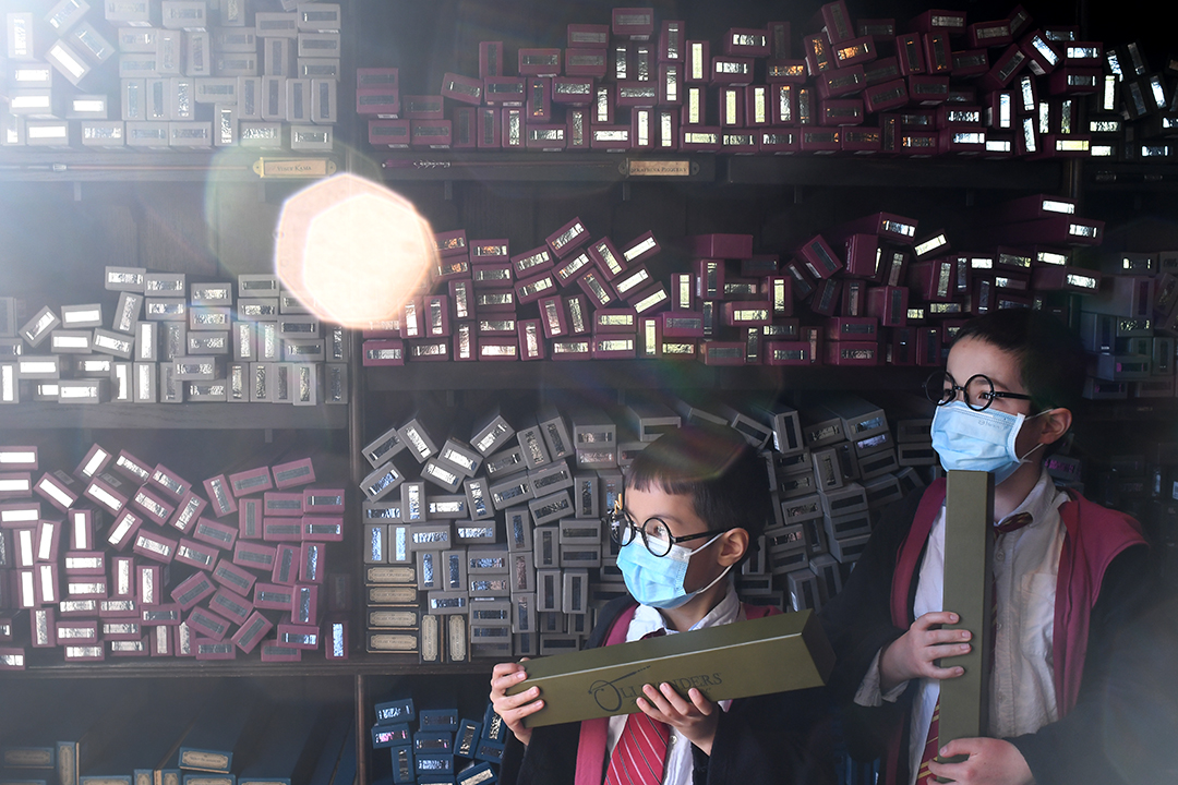 Two boys pose in Hogwarts robes inside Ollivanders wand shop in Hogsmeade Wizarding World of Harry Potter at Universal Studios Hollywood