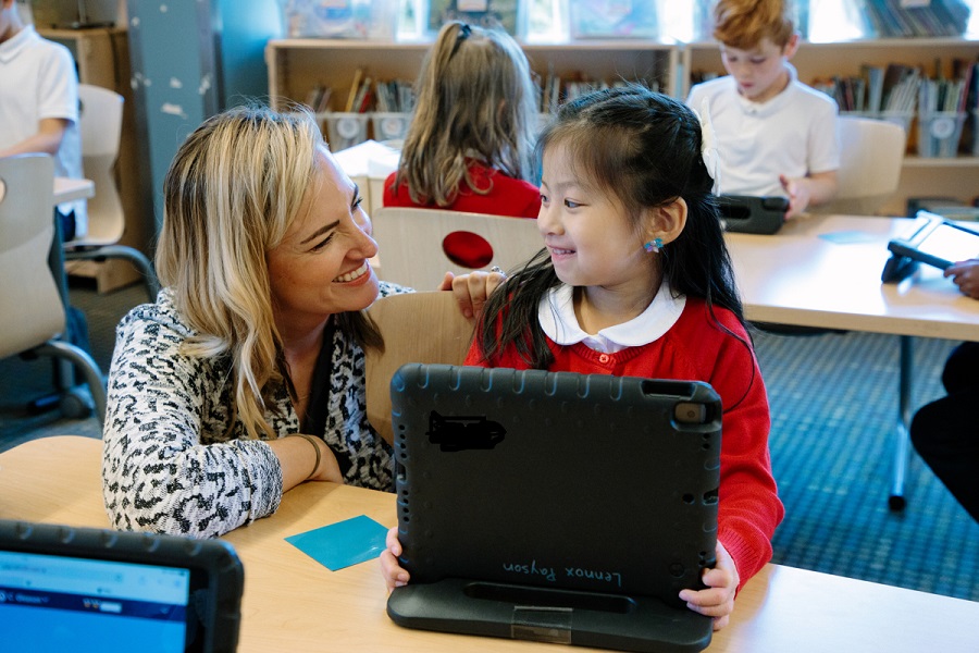 Young student at the Ephiphany school works on a laptop and is helped by her math teacher