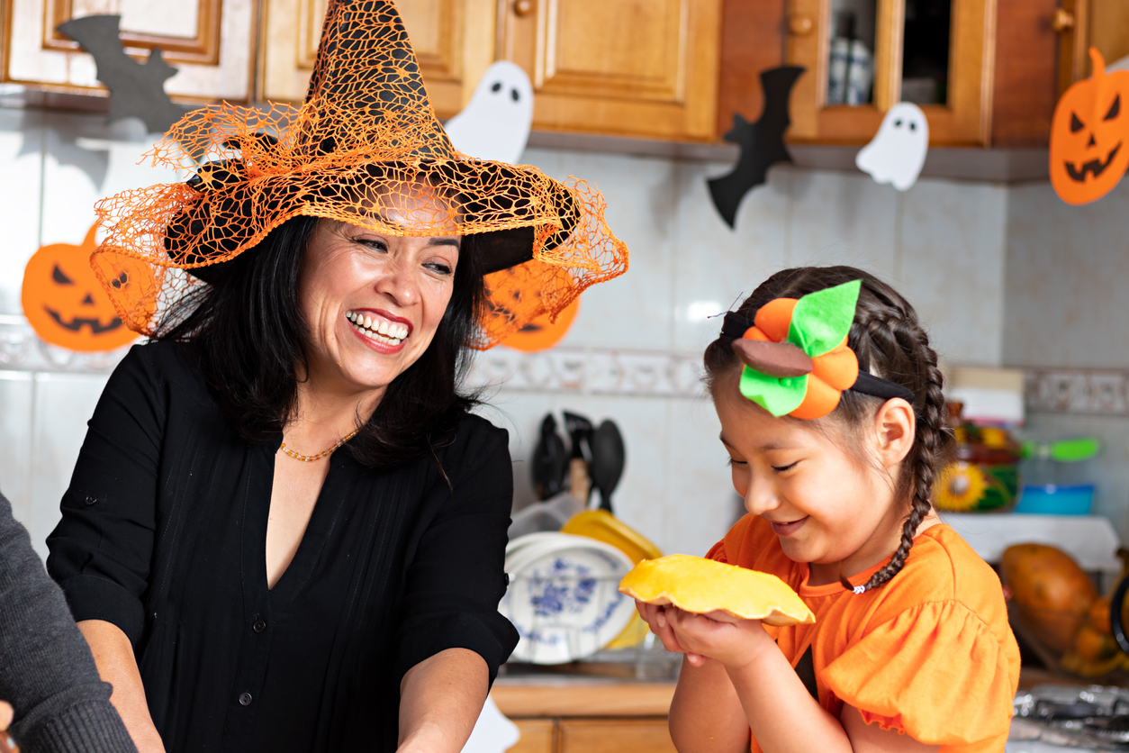 A happy mom and daughter wearing costumes in their kitchen prepare Halloween snacks and have fun together