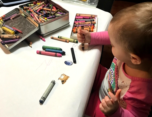 Toddler drawing with crayons on a giant piece of butcher paper on a table