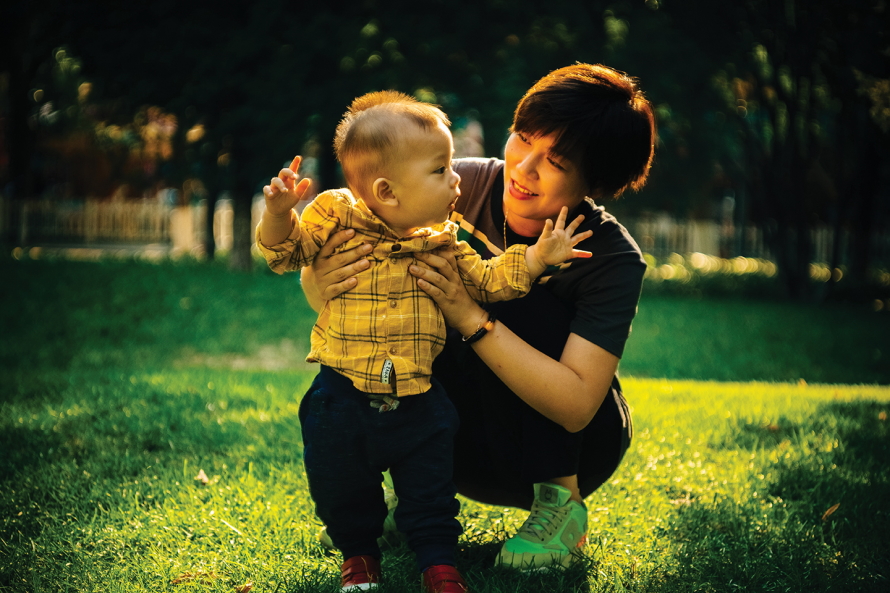 Mom helping a baby stand in the grass