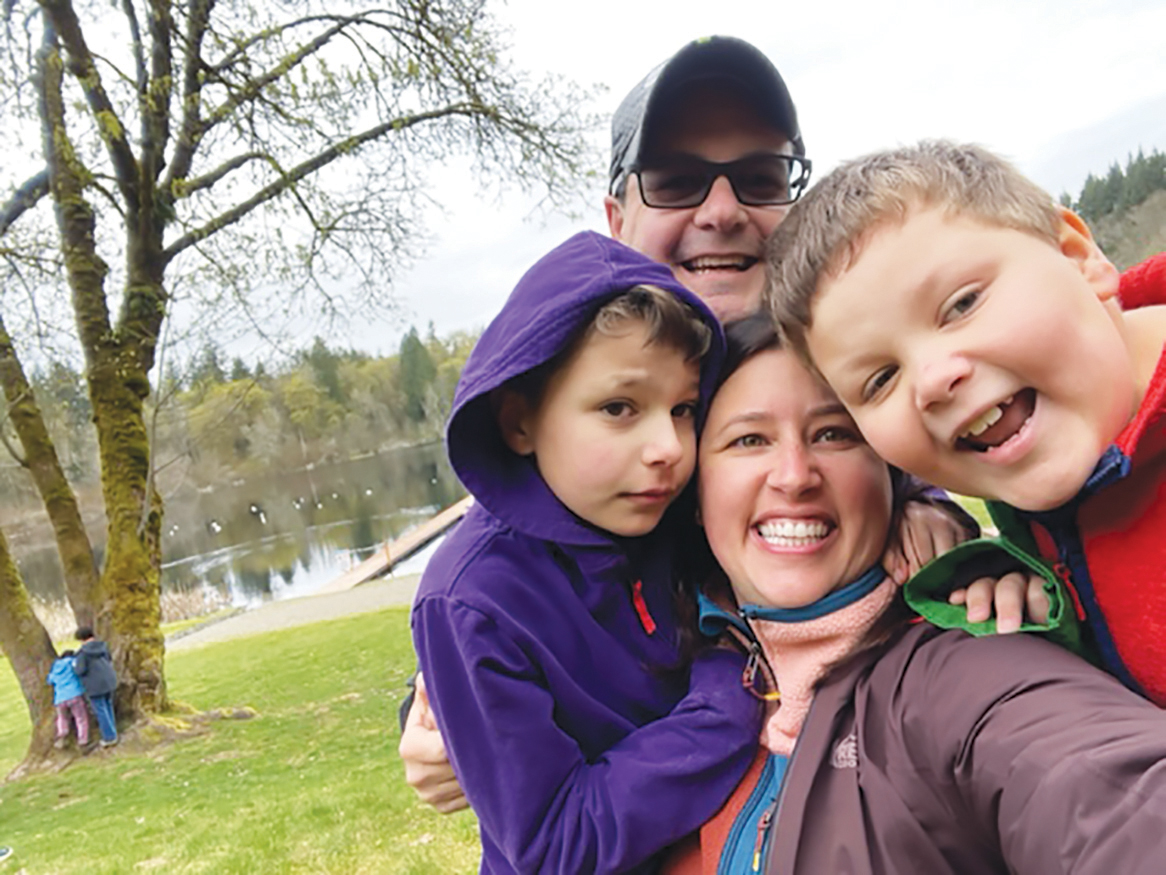 Mom, dad, and two kids smiling and standing by a lake