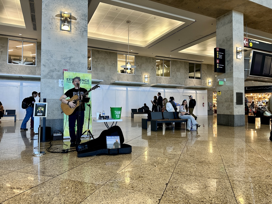 A man, Joshua Red Uttech, playing the guitar and singing at SEA airport