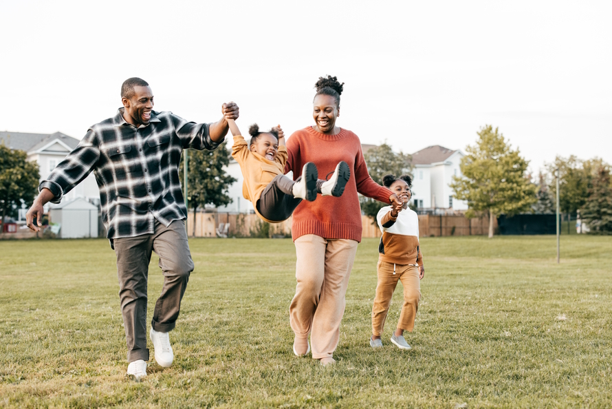 Family in a field, parents swinging young child in the air