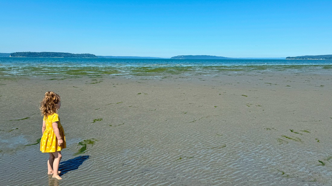 Young girl on Jetty Island beach wearing sunglasses at low tide on a summer day