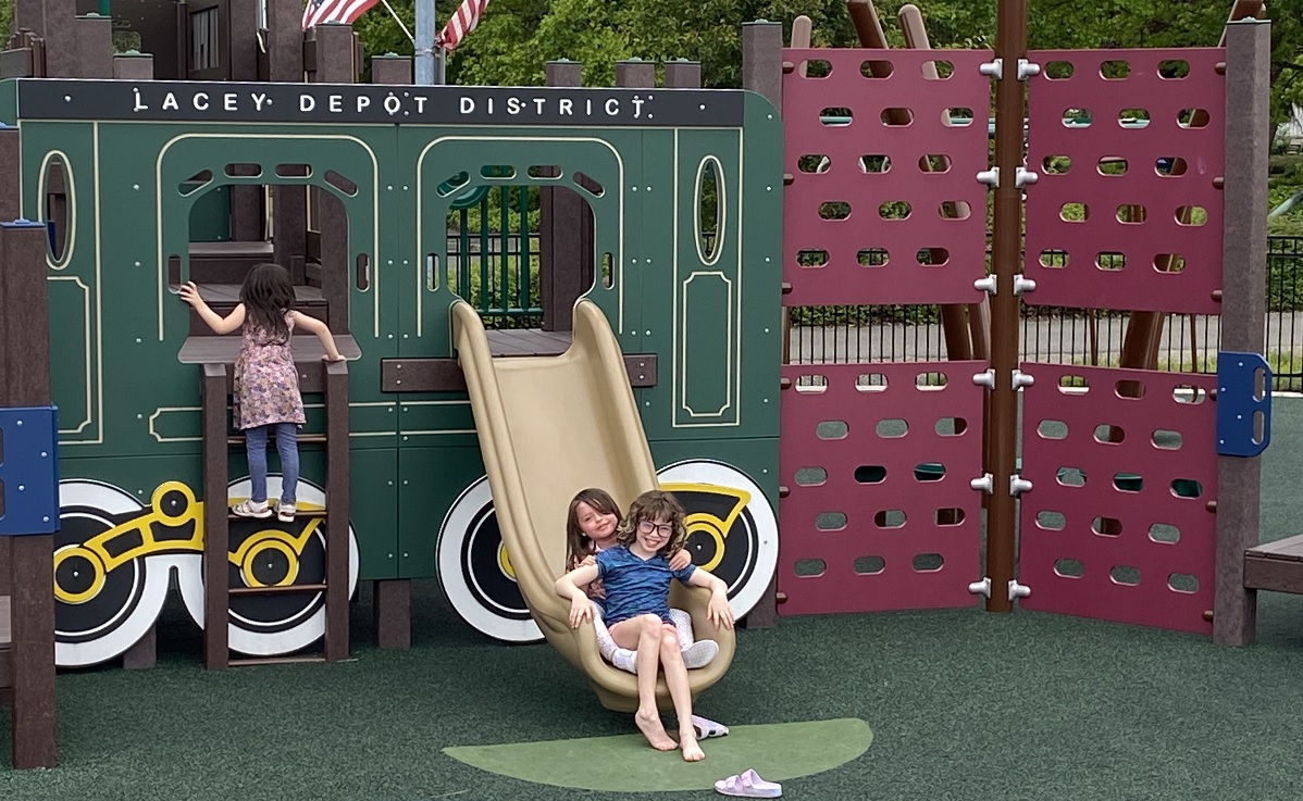 Kids play on a train car play element at Lacey Depot District new playground South Sound