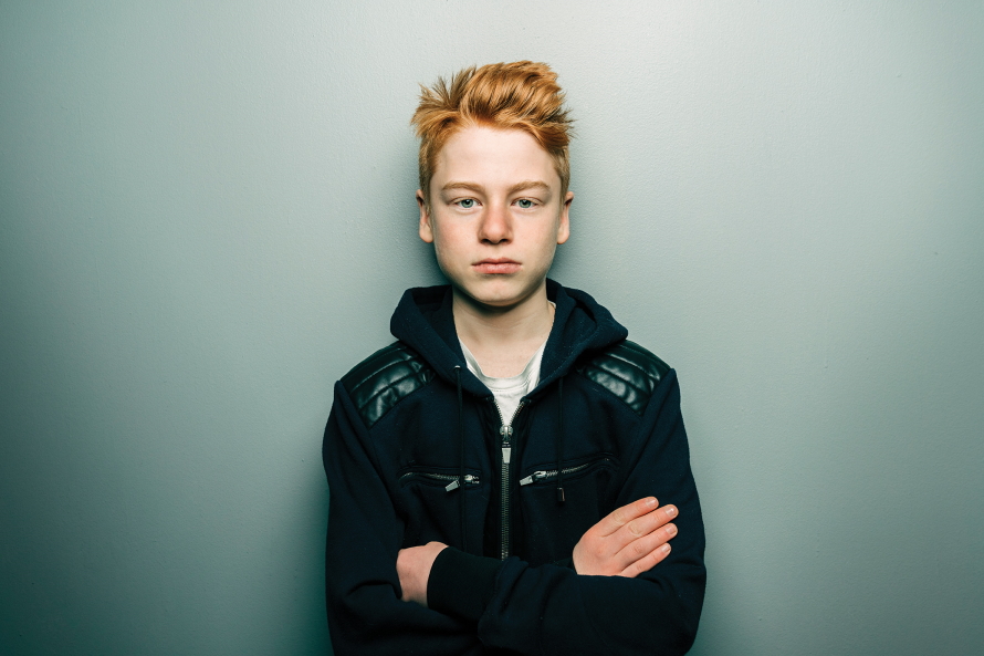 Tween boy looking annoyed at the camera with his arms crossed