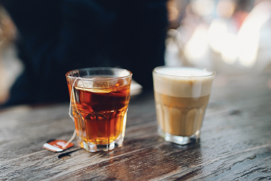 Two shot glasses on a wooden table. One is full of tea, the other coffee.