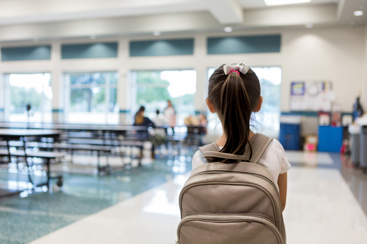 rear view of a girl with a backpack entering a relatively empty school cafeteria