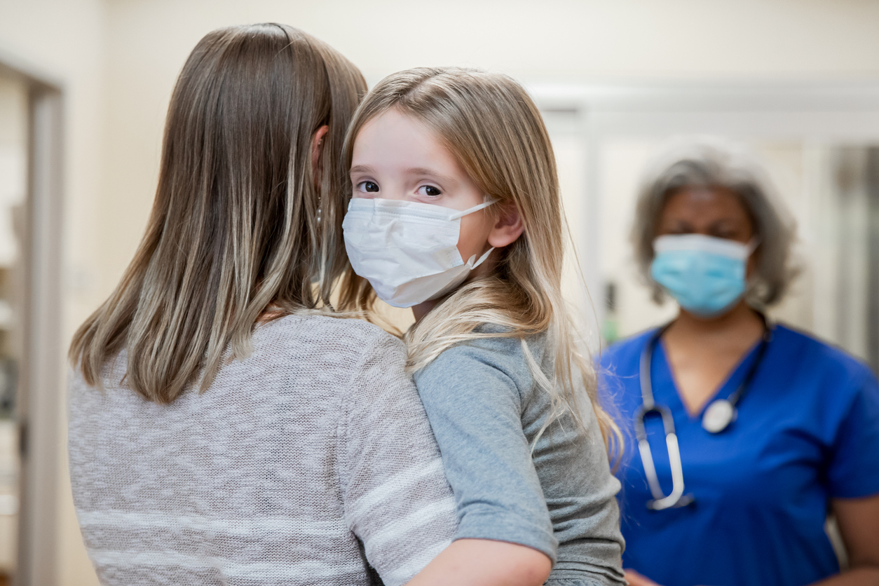 Mom holding young girl wearing mask in a hospital