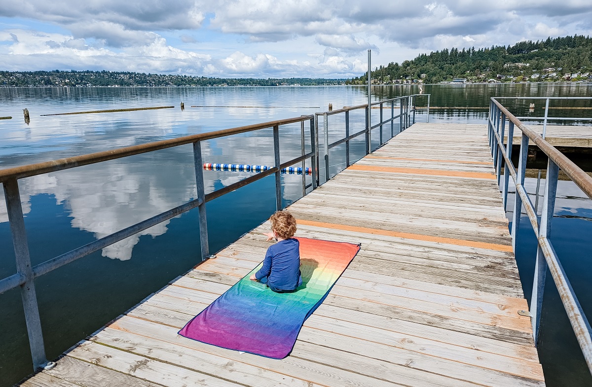 A boy sits on a towel on the dock at Kennydale Beach Park having a picnic with his family