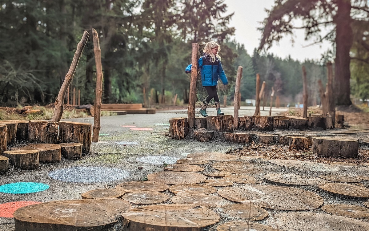 A young girl in a blue jacket plays on the nature features at updated Swan Creek park in Tacoma Washington fun for kids families