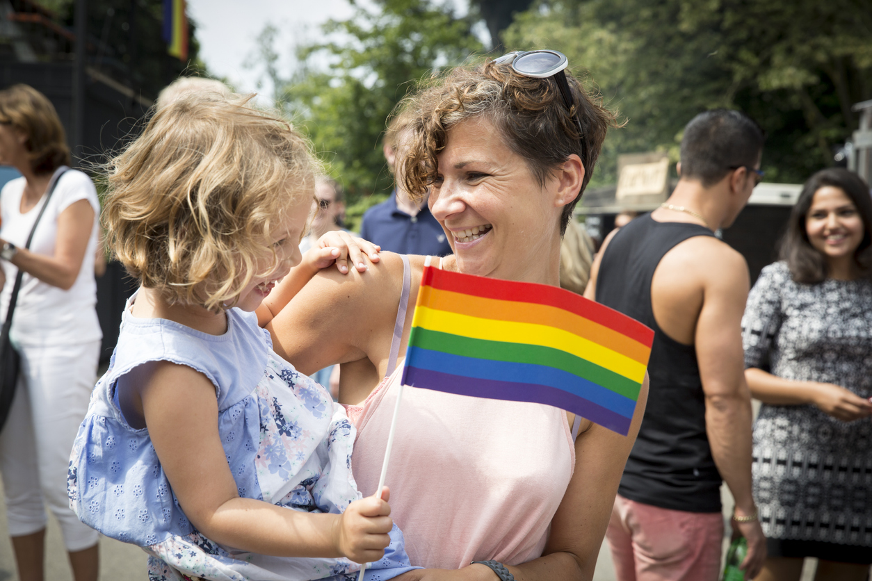 mother hugging her daughter at a pride parade with daughter holding the pride flag