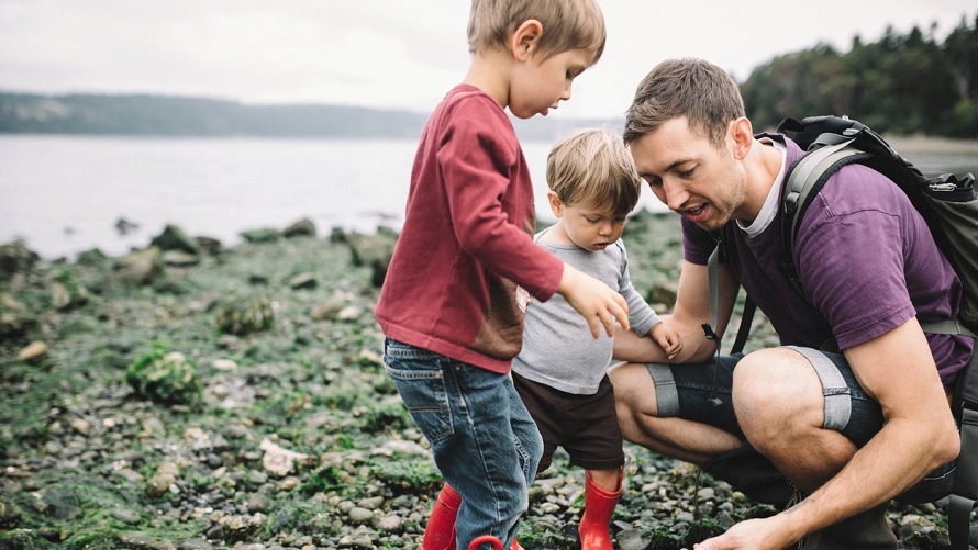 Dad and two little kids looking at rocky beach and tide pool finds