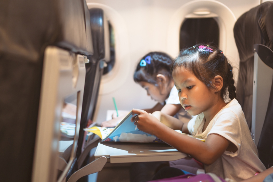 Two kids on an airplane looking at activity books