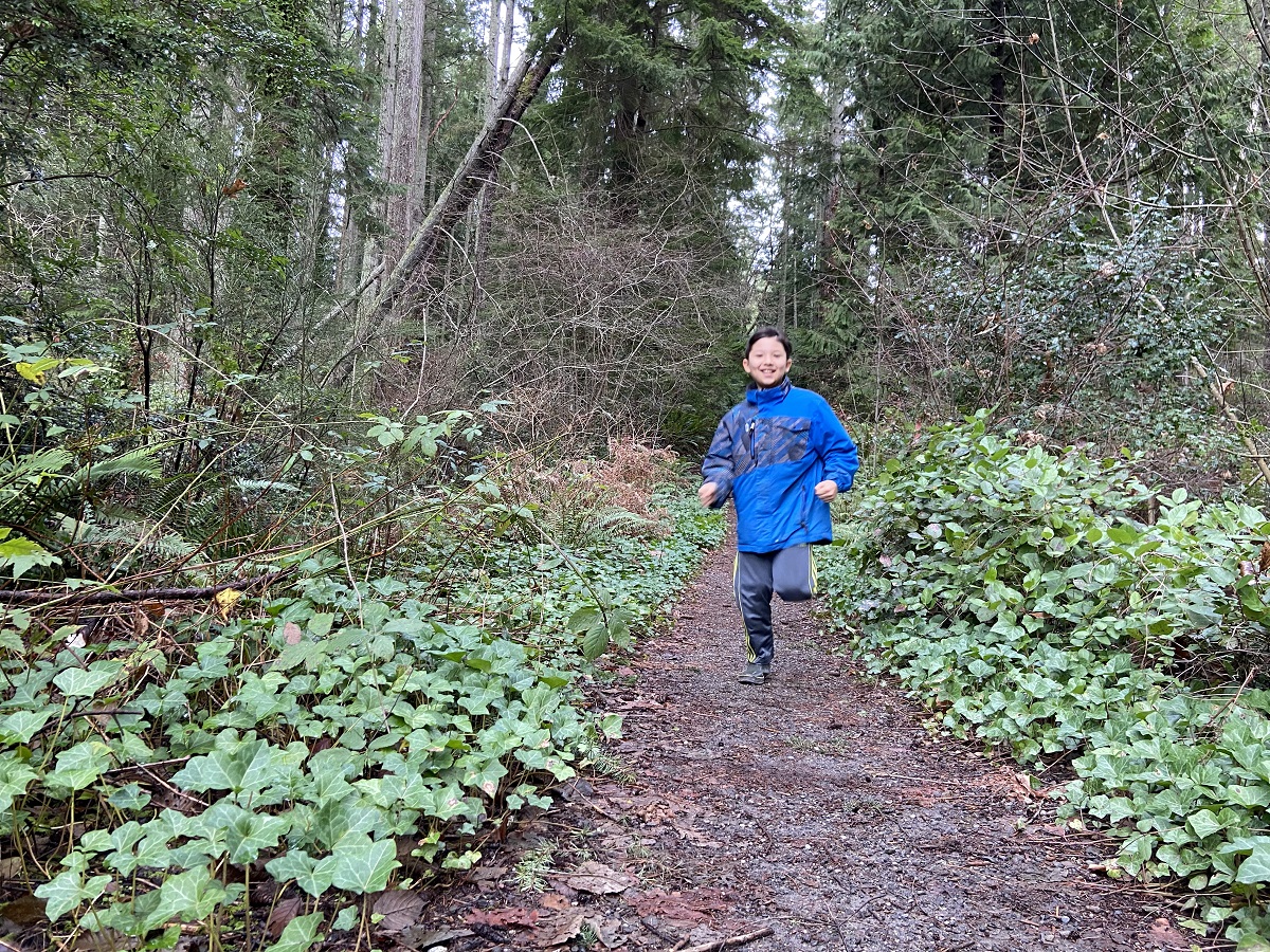 Happy kid in blue jacket running on a forested trail on Bainbridge Island near Gazzam Lake Nature Preserve
