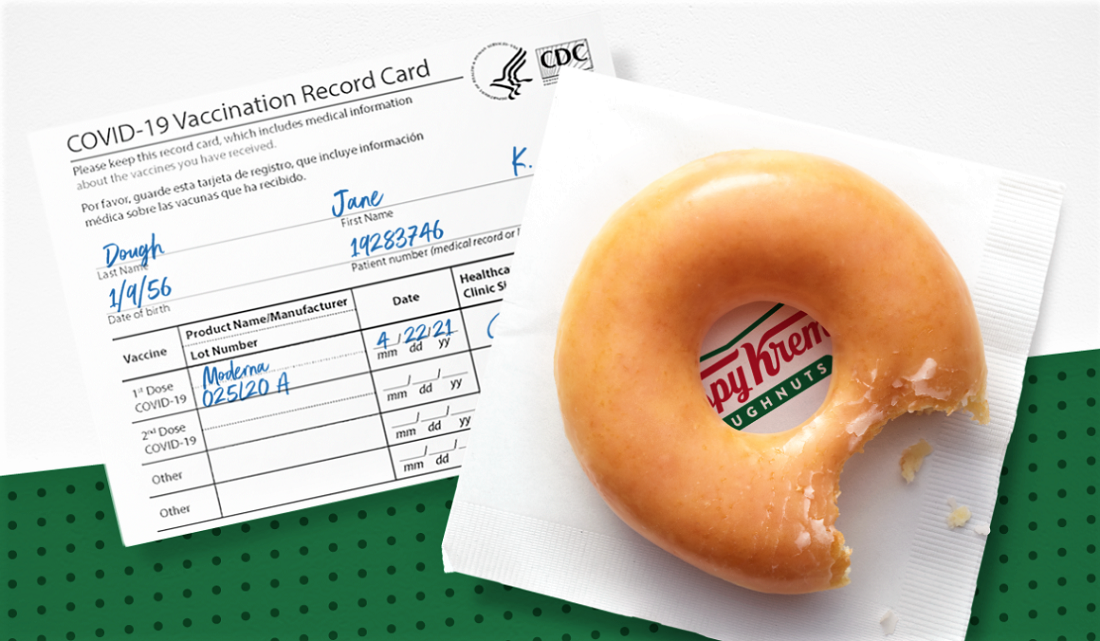 A sample COVID 19 vaccine card alongside a Krispy Kreme glazed doughnut sitting on a napkin; doughnut chain offering free doughnuts to vaccinated individuals