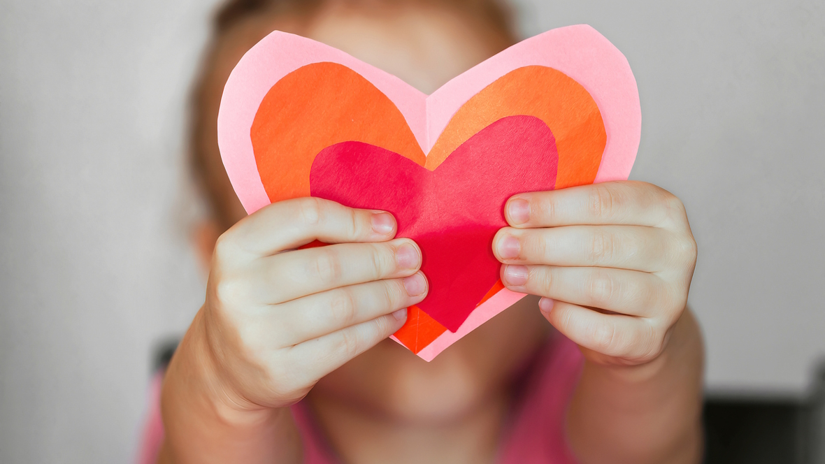 child hands holding up a paper heart shaped valentine