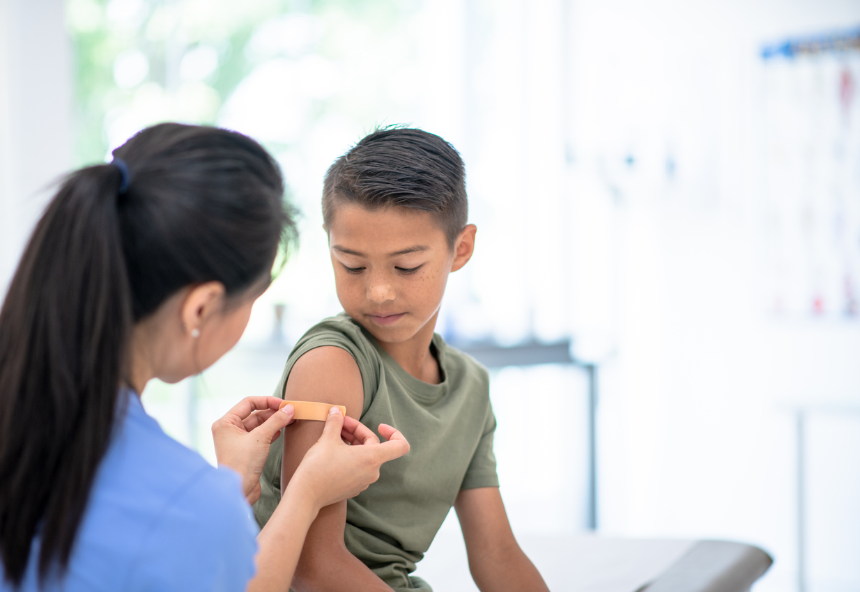 Young boy getting a shot and looking down at his arm