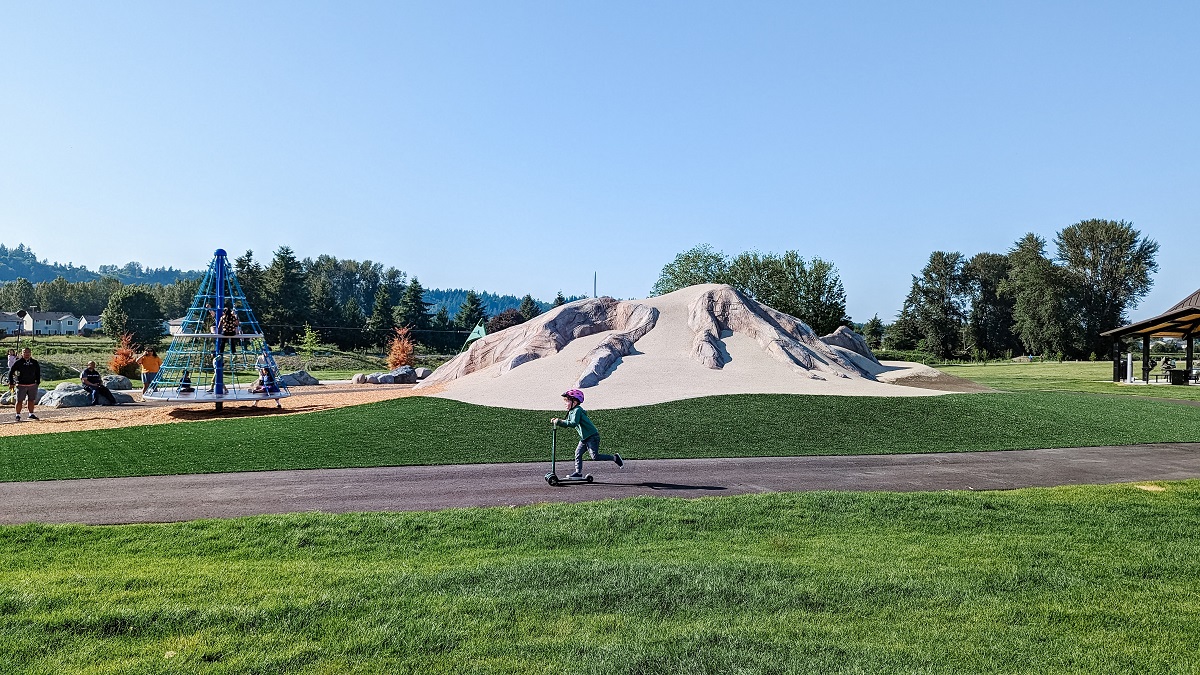 A young boy rides a scooter along a smooth paved path at the newly updated playground at Kent’s Van Doren’s Landing Park, near Seattle
