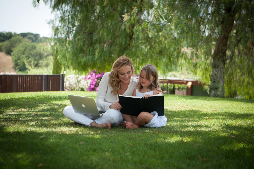 Jessica Joelle Alexander, and her daughter Sophie, sitting in the grass with a book and a computer