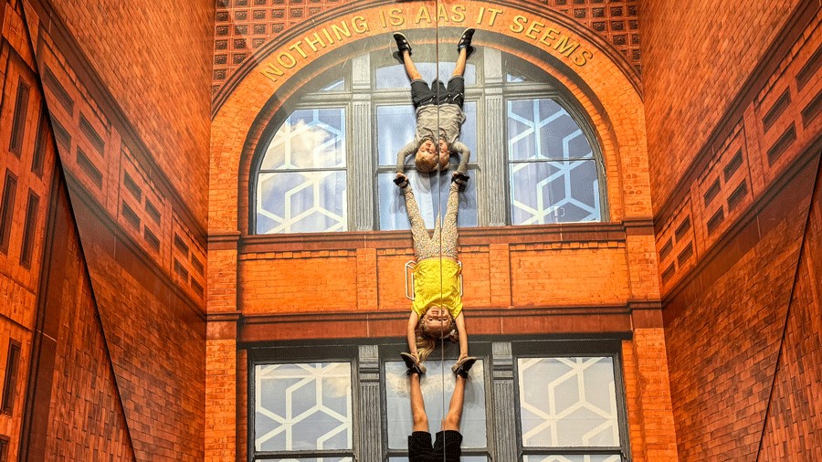 Three kids hold onto each other’s feet at Museum of Illusions Seattle to look upside down