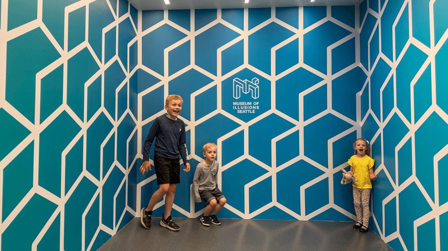 Three kids pose in a room at Museum of Illusions and appear different in size