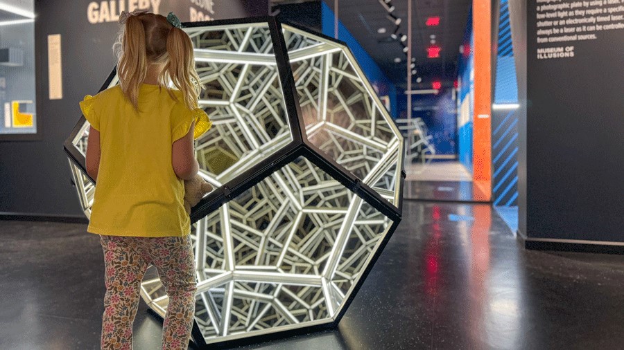 Young girl looks into geometric mirror display in the dark gallery at Museum of Illusions