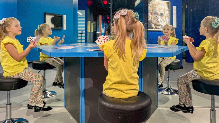 Young girl plays a card game with herself using mirrors at Museum of Illusions