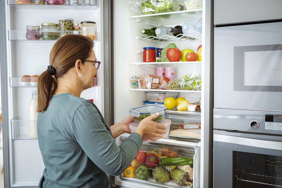 Woman putting containers of food into the fridge to help reduce food waste