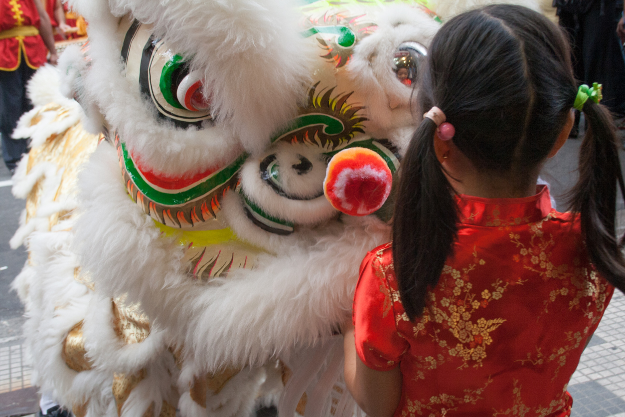 A young Asian girl watches a lion dance at a celebration of Chinese New Year